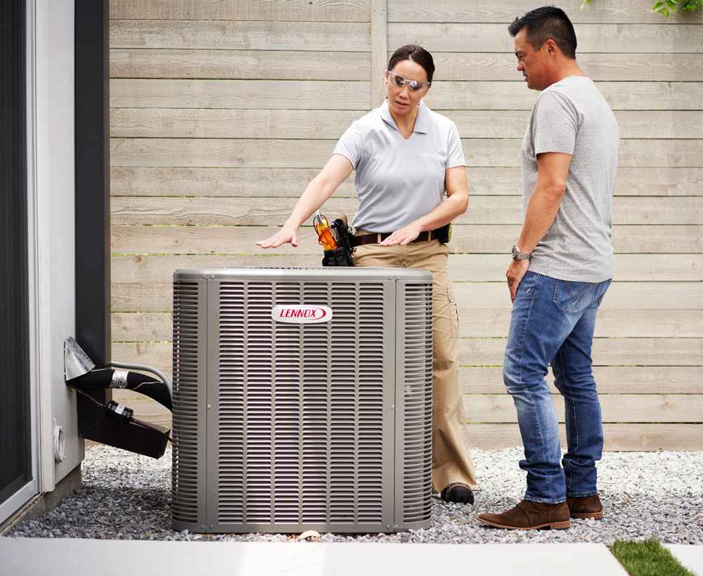 Technician and homeowner standing next to new Lennox HVAC unit outside home. Technician explaining system to homeowner.